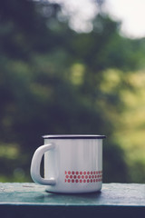 White enamel mug on the window sill in front of a blurry forest background