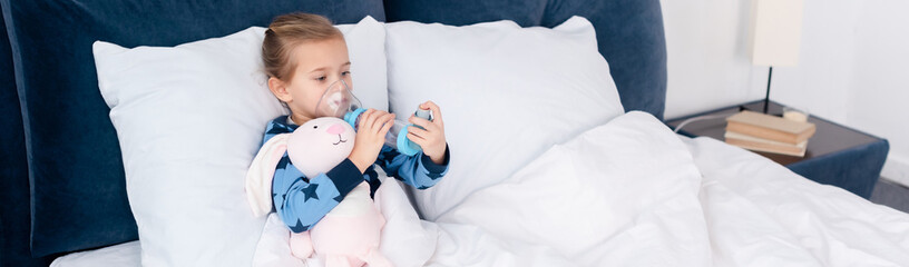 panoramic shot of sick kid using inhaler with spacer near bunny toy