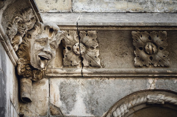 Stone face sticking out tongue, detail of an ancient cloister in Portugal