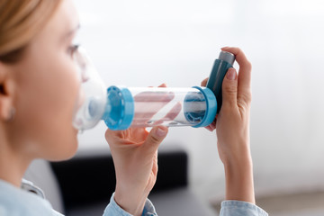 selective focus of asthmatic woman using inhaler with spacer - obrazy, fototapety, plakaty