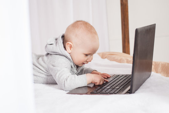  A little kid plays with a laptop, presses buttons, enjoys a new toy. A boy in a gray suit sits on a brown white canopy bed.