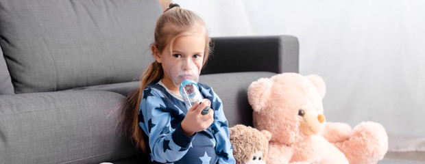 panoramic of sick kid using inhaler with spacer near soft toys