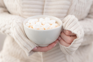 Obraz na płótnie Canvas A Cup of hot chocolate and marshmallow close-up in the hands of a girl in a knitted light jacket.