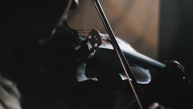 Young woman fiddler practice playing the violin at home in harsh daylight, low light scene, detail of instrument in moody scene, focus on bridge and bow