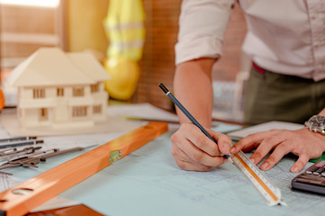 Close up of male architect hands measuring and making model house on the desk at sunset. Engineer, Engineering, Architecture, Design, Planning, Occupation concept.