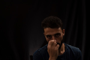 Portrait of young brunette Indian Kashmiri man in casual tee shirt playing cards on a casino poker table in black copy space studio background. lifestyle and fashion.