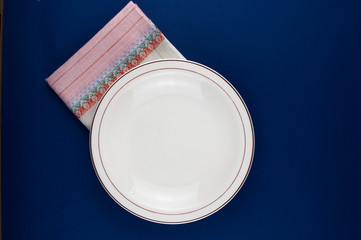 Top view of empty white dish and colorful tablecloth on blue background with copy space.