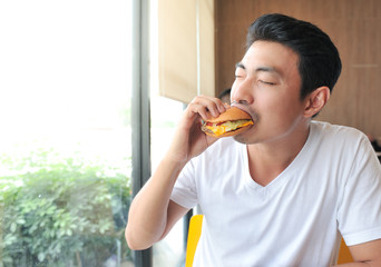 Asian man is biting a burger,A man enjoy eating with burger in his hand,Burger is hight calories food,Selective focus