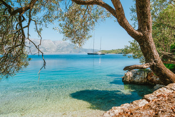 Summer vacation in Greece. Sea bay view framed with old olive tree and luxury yacht in lagoon in a distance