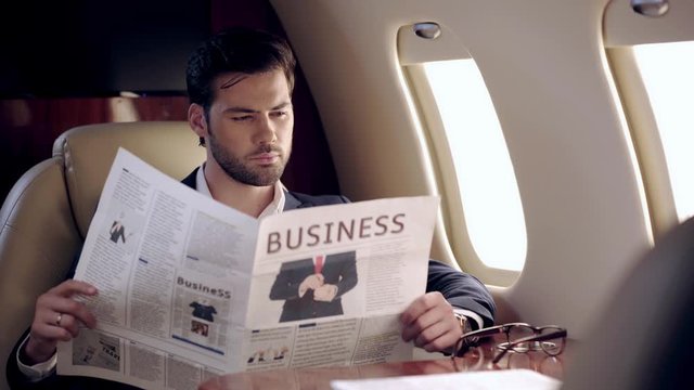 concentrated businessman reading newspaper while traveling by plane