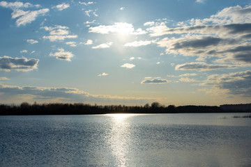 The sun in the cloudy sky. Sunset by the river near the forest.