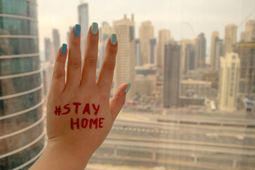 Woman hand on a window with "Stay Home" writing on a blurred Dubai skyscrapers background. Stay Home call during COVID-19 Outbreak.