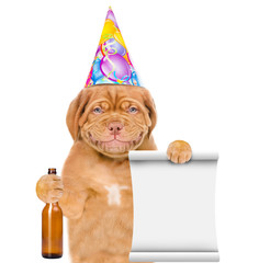 Smiling puppy wearing birthday cap holds glass bottle and empty list. isolated on white background