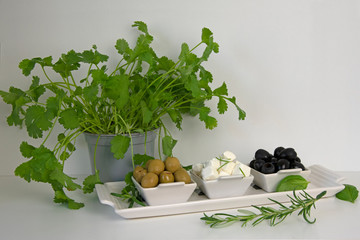 Platter of olives, feta cheese and rosemary on wooden board with coriander plant