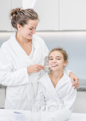 Fototapeta premium Smiling woman teaching her young daughter how to brush teeth with toothbrush