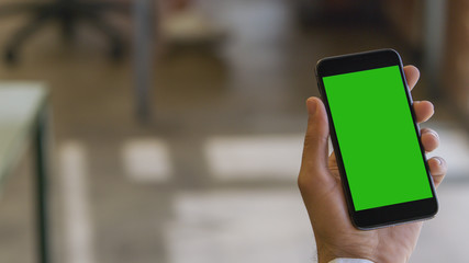 Man's hand holding a smartphone (green screen)