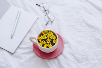 Сup with yellow flowers inside, on a white bed in the morning with notepad and pen. Spring background