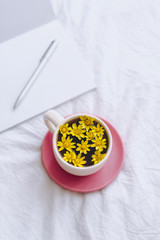 Сup with yellow flowers inside, on a white bed in the morning with notepad and pen. Spring background