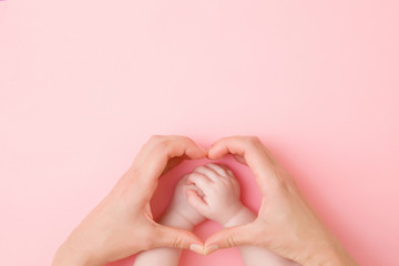 Fototapeta Heart shape created from young mother hands. Infant arms in middle. Light pink table background. Pastel color. Lovely emotional, sentimental moment. Empty place for text, quote or sayings. Top view. obraz