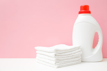Obraz na płótnie Canvas Plastic liquid detergent bottle and white towels. Fabric softener. Regular washing. Front view. Closeup. Laundry concept. Empty place for text or logo on pastel pink background.
