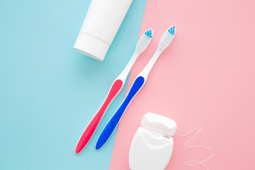 White tube of toothpaste, two toothbrushes and container of dental floss on pastel blue pink table background. Male and female teeth hygiene concept. Closeup. Top down view. Two sides.