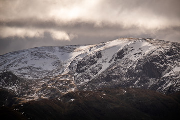 Fototapeta na wymiar Sun breaking through clouds on the snow covered Eastern Face of Dolywaggon Pike, Lake District, UK