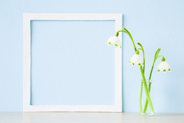 Fresh snowdrops in glass vase on table at light pastel blue wall. First messengers of spring. Empty...