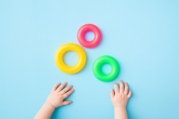 Baby hands playing with green, yellow and pink plastic rings on light blue table background. Pastel color. Closeup. Toys of development for little kids. Top down view.