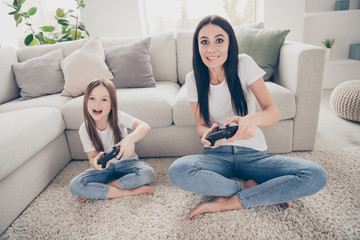 Obraz premium Full length photo of excited energetic mommy small kid sit legs crossed carpet play video game want win wear white t-shirt denim jeans in room house indoors