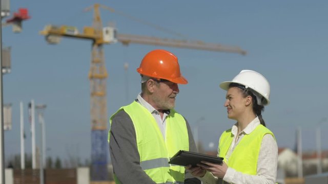 Elderly man and a young woman with a tablet in hands at a construction site. Builders discuss working issues.