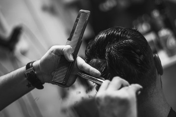 Peluquero profesional efectuando con tijera corte de pelo moderno masculino en salon de peluqueria