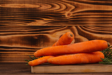 Close-up of fresh carrots and rosemary on cutting board, rustic wooden background