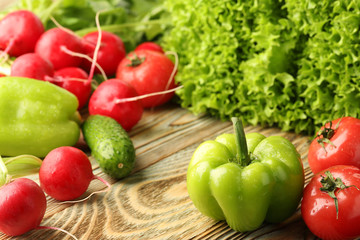Assorted fresh vegetables, tomato, radish, cucumber, bell pepper and lettuce, new crop on a wooden background, closeup.
