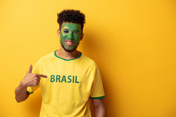 smiling african american football fan with painted face pointing at t-shirt with brazil sign on...