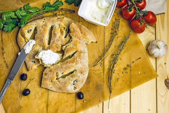 Homemade flat french Fougasse bread on a wooden table, near olives, spicy herbs, tomatoes. Top view,copy space