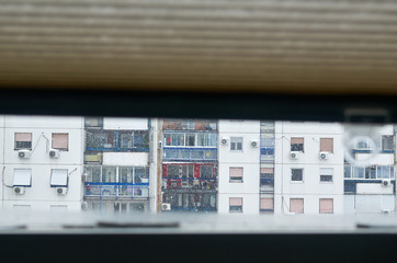 View through a window with a slightly raised blind to a next residential building during a snowy...