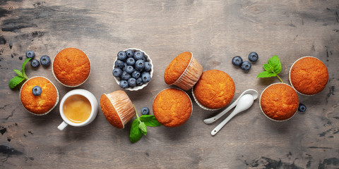 Muffins or capcakes with blueberries and mint, a cup of coffee on a wooden background. Top view