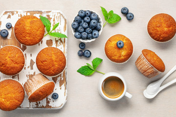Muffins or capcakes with blueberries and mint, a cup of coffee on a wooden background. Top view