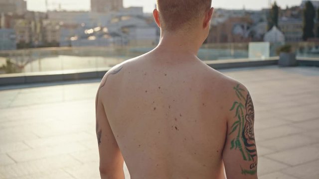 shirtless man with tattoos smiling and holding nunchaku