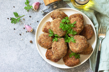 Homemade juicy delicious meat cutlets in plate, meatballs from minced meat on a gray stone table. Top view flat lay background. Copy space.