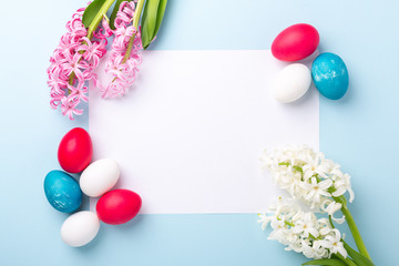 Spring mockup with Easter eggs, hyacinths and blank of white paper on blue background. Easter concept. Copy space. Top view