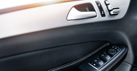 Car interior details of door handle with window control buttons and adjustments. Luxury close up or car window controls system.