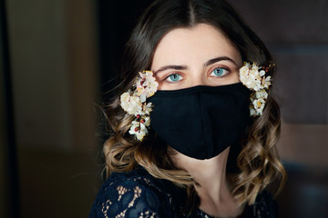 Young beautiful woman in black protective mask decorated with spring flowers, stay isolation at...