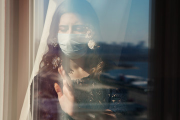 Fototapeta premium Young pretty woman in medical mask decorated with spring flowers stay isolation at home for self quarantine. Concept home quarantine, prevention COVID-19, Coronavirus outbreak situation