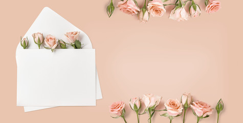 Blank envelope with rose flowers on peach color background. Top view of spring roses and rosebuds....