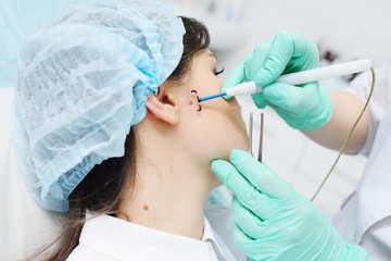 A young woman doctor dermatologist surgeon holds a radio wave knife in the background of a young...