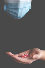A man in a protective medical mask holds multi-colored antiviral pills in his hand during the pandemic