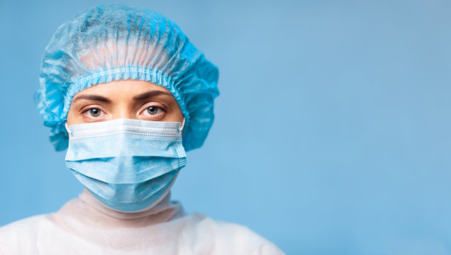 portrait of a young woman doctor in a protective mask on her face and a medical cap, on a blue background. copy space