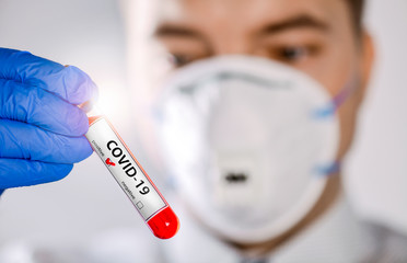 Doctor holding a positive blood test-tube result for the new Coronavirus in blue gloves.