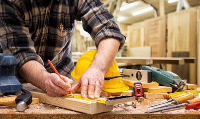 Close-up. Carpenter with pencil and carpenter's square draw the cutting line on a wooden board. Construction industry, carpentry workshop.